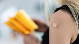 Frau mit geimpftem Arm und Impfpass in der Hand
