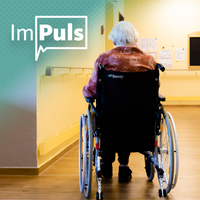Im Gang eines Pflegeheims sitzt eine alte Frau im Rollstuhl