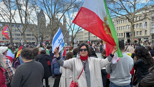 Person steht mit Flagge in der Hand von weiteren Personen am Neumarkt 