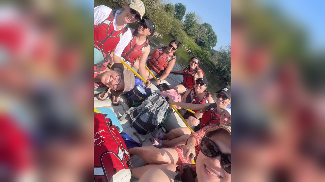 Eine Gruppe weiblicher gelesener Personen lächelnd auf einem Paddelboot