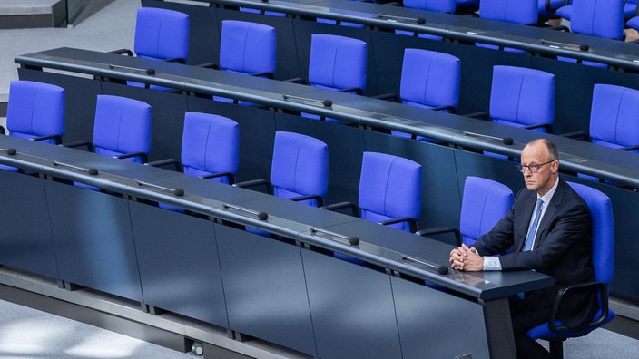 Weite Aufnahme von Friedrich Merz allein im Bundestag sitzend