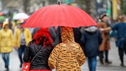 Zwei Karnevalisten laufen mit einem roten Regenschirm durch die Straßen