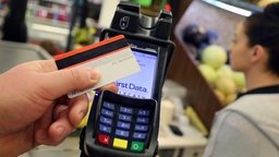 Eine EC-Karte wird an den Bezahl-Terminal an der Kasse eines Supermarktes gehalten.