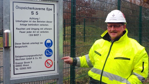 Hans Peter Jackelen vor einem Zaun, links Schild über Ölspeicherkaverne