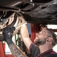 Kfz-Mechatroniker kontrolliert in einer Werkstatt den Unterboden an einem PKW.
