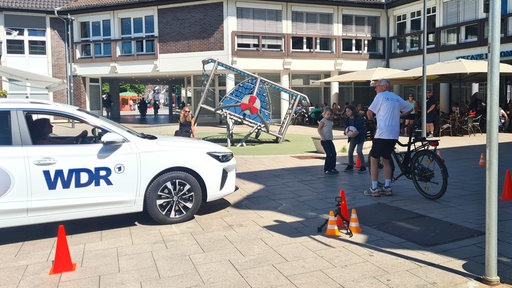 Gestellte Verkehrsszene mit Auto, Fußgängern und Radfahrer