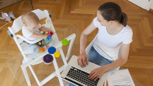 Frau sitzt mit Baby und Laptop am Tisch