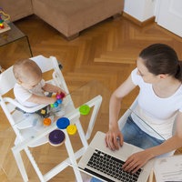Frau sitzt mit Baby und Laptop am Tisch