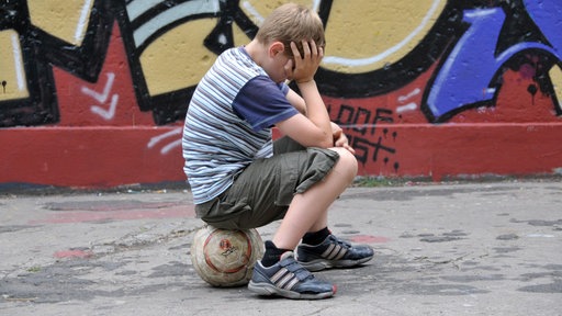 Junge mit Fußball im Grafitti-bunten Hinterhof eines alten Mehrfamilienhauses