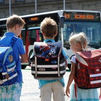 Vier Kinder mit Tonistern auf dem Rücken warten auf den Bus