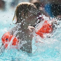 Einer junger Badegast mit Schwimmflügeln kühlt sich hohen Temperaturen in einem Schwimmbad ab.
