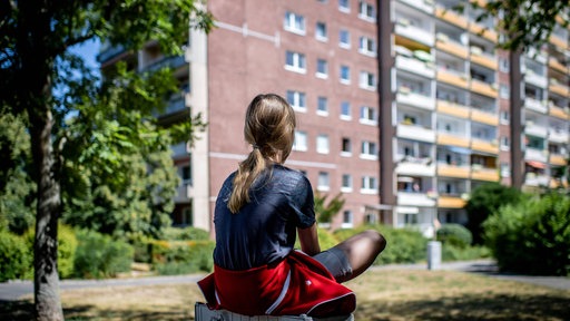 Ein Kind sitzt vor einem Plattenbau (Symbol)