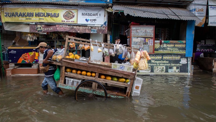 Indonesien, Jakarta: Ein Obst- und Gemüsehändler zieht seinen Verkaufskarren durch eine überflutete Straße.
