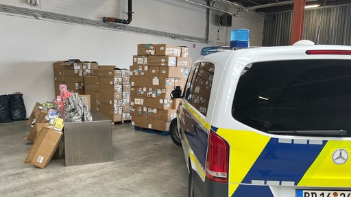 Das Bild zeigt ein Polizeiwagen sowie viele Kartons mit sichergestellten Vapes.