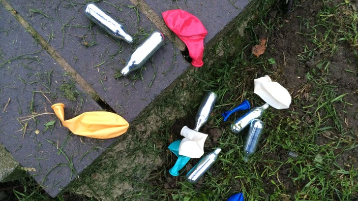 Lachgas-Kartuschen und Luftballons liegen auf dem Boden in einem Park