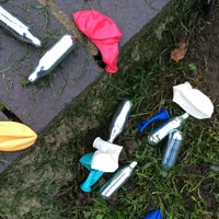 Lachgas-Kartuschen und Luftballons liegen auf dem Boden in einem Park