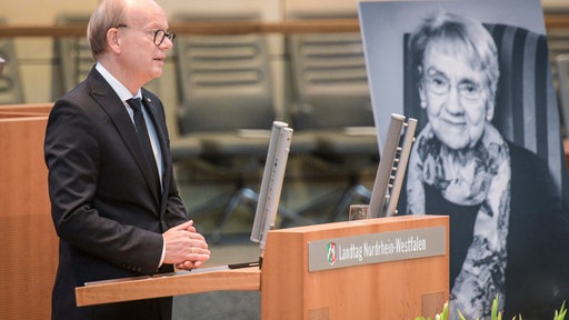 André Kuper steht vor einem Bild von Ingeborg Friebe auf ihrer Gedenkfeier