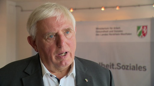  Karl-Josef Laumann spricht im WDR-Interview, im Hintergrund ist das Logo seines Ministeriums zu sehen