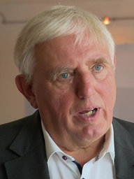  Karl-Josef Laumann spricht im WDR-Interview, im Hintergrund ist das Logo seines Ministeriums zu sehen