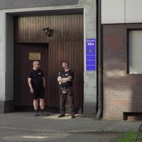 Ein braunes Holztor, davor zwei Männer, die die Tür bewachen. 