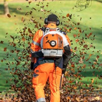 Ein Arbeiter beseitigt Laub in einem Park mit einem Laubbläser
