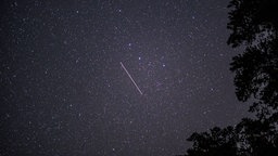 Aufnahme von einem Sternenhimmel und einer Sternschnuppe bei Nacht.