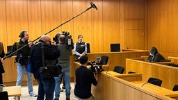 Angeklagter sitzt umringt von Jourrnalisten mit Kameras im Gerichtssaal 