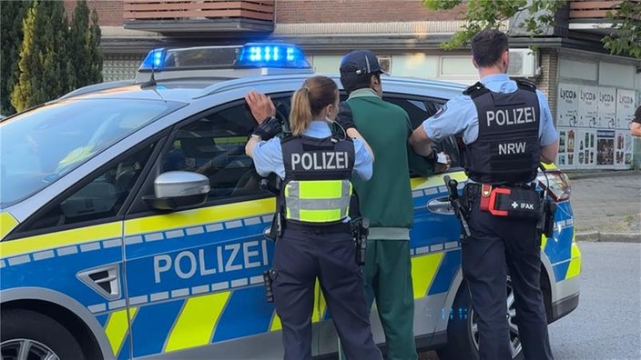 Verdächtiger wir von Polizisten gegen ein Auto gelehnt und festgehalten