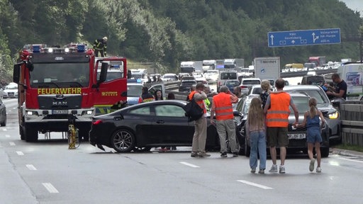 Mehrere Personen stehen vor der Unfallstelle und einem Feuerwehrauto 