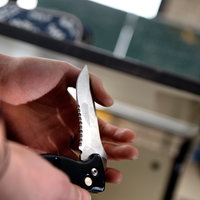 Eine Person hält in einem Klassenzimmer ein Klappmesser in der Hand.