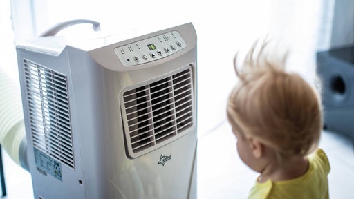 Ein Kind steht vor einer mobilen Klimaanlage in einer Wohnung