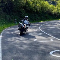 Blick auf die L218 im Kreis Düren, auf der Fahrbahn sind ellipsenförmige Markierungen, zwei Motorräder fahren in eine Kurve