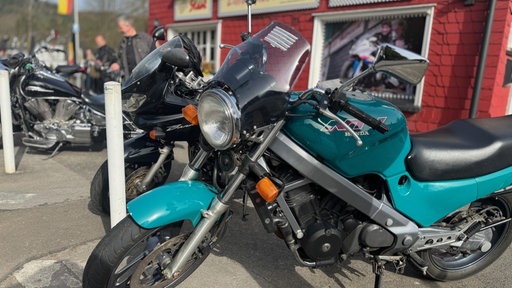 Ein türkises Motorrad steht auf einem Parkplatz