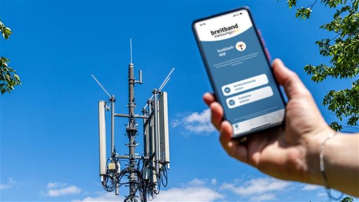 Ein Handy wird in Richtung eines Mobilfunkmastes gehalten
