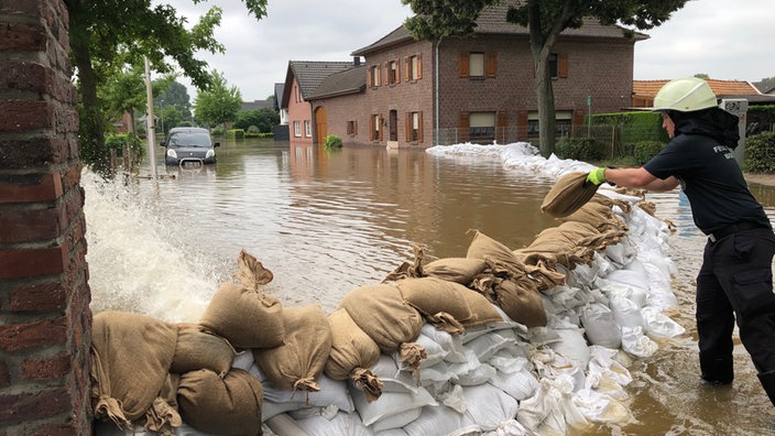 In Ophoven versuchen Mitarbeiter der Feuerwehr die Wassermassen mit Sandsäcken einzudämmen