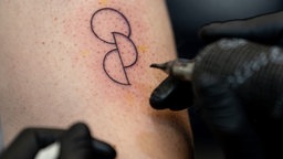 Ein Tätowierer sticht einem Kunden ein Organspende-Tattoo