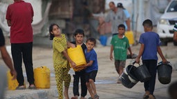Drei Kinder tragen einen Wassertank