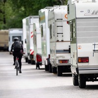 Ein Radfahrer fährt in einer Straße an geparkten Wohnmobilen und Wohnwagen vorbei