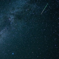 Eine Sternschnuppe leuchtet neben der Milchstraße am Himmel
