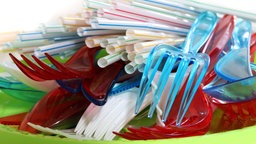 Plastikbesteck farbig und weiss mit Trinkhalmen auf einem Plastikteller