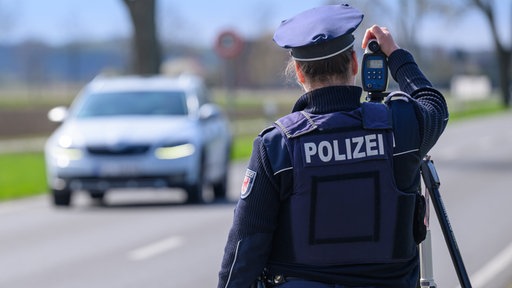 Eine Polizistin steht am Straßenrand und misst die Geschwindigkeit des entgegenkommenden Autos