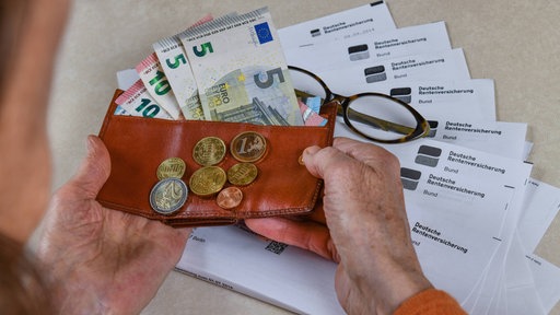 Rentnerin hält Portemonnaie mit Geld in den Händen und Rentenbescheide liegen auf dem Tisch