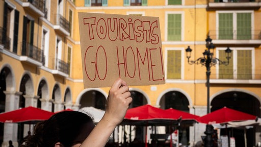 Eine Frau hält ein Schild mit der Aufschrift "Tourists Go Home" hoch