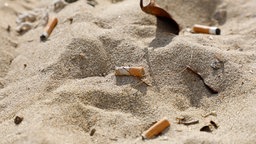 Zigarettenstummel liegen im Sand am Strand 