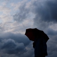 Ein Mann geht mit einem Regenschirm vor aufziehenden dunklen Wolken spazieren.