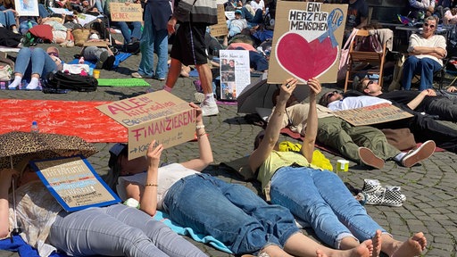 Menschen liegen auf dem Boden und halten Plakate hoch