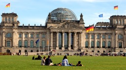 Menschen sitzen auf der Wiese vor dem Reichstagsgebäude in Berlin.