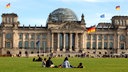 Menschen sitzen auf der Wiese vor dem Reichstagsgebäude in Berlin.