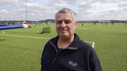 Schiedsrichter Reiner Gillitzer steht lächelnd auf einem Fußballfeld