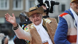 Herbert Reul, Innenminister NRW, winkt beim Rosenmontagszug den Karnevalisten zu. 